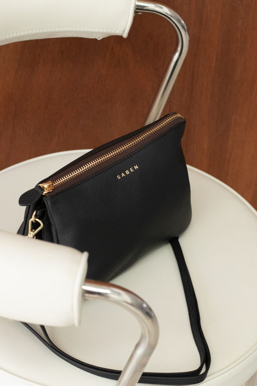 Black handbag with gold zipper on a white chair
