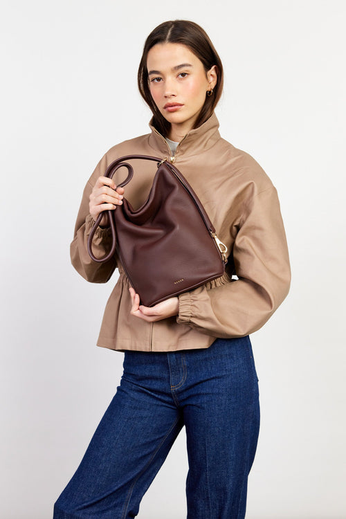 Woman holding a brown leather handbag against a plain background