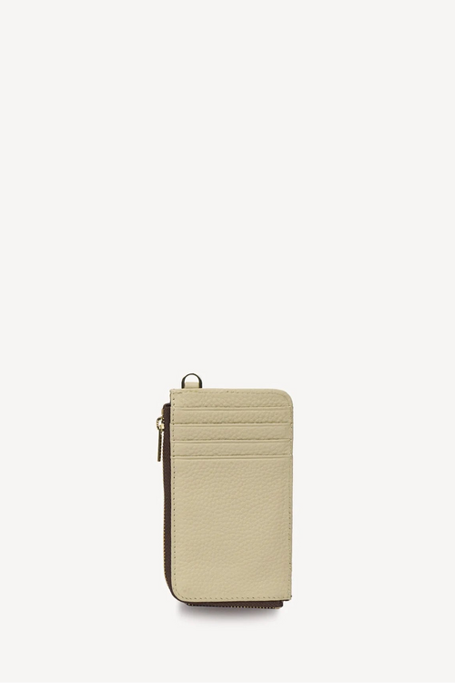 A slim, vertical beige leather card holder or wallet with a gold-tone zipper pull and metal ring detail, shown on a plain off-white background.
