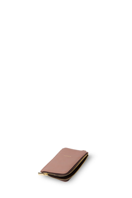 A slim, zippered leather wallet in a dusty rose pink color with gold hardware and a subtle gold logo embossed on the front, set against a solid white background.