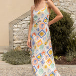 Woman wearing a colorful patterned dress standing outdoors against a stone wall.