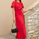 Woman in a red dress standing against a beige wall with stone steps.