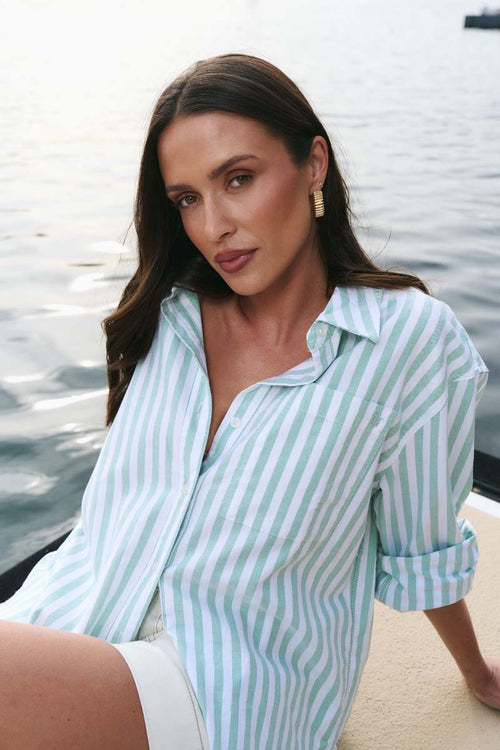 Woman wearing a light blue and white striped shirt by a body of water.