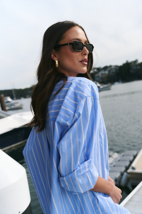 Woman wearing a blue striped shirt by a waterfront with boats in the background