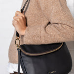 Person wearing a black crossbody bag with a visible brand logo against a white background