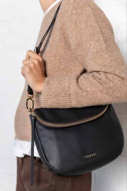 Person wearing a black crossbody bag with a visible brand logo against a white background