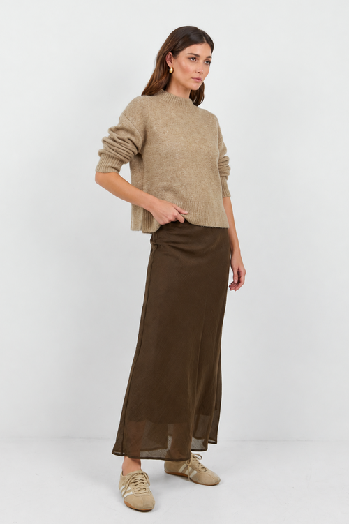 Woman wearing a beige sweater and brown skirt on a white background