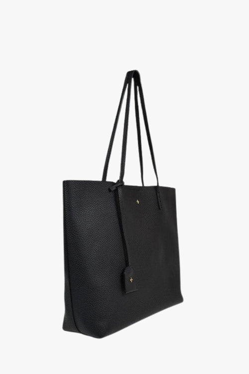 A black pebbled leather tote bag with long shoulder straps and a small gold cross logo on the front, shown against a plain white background.