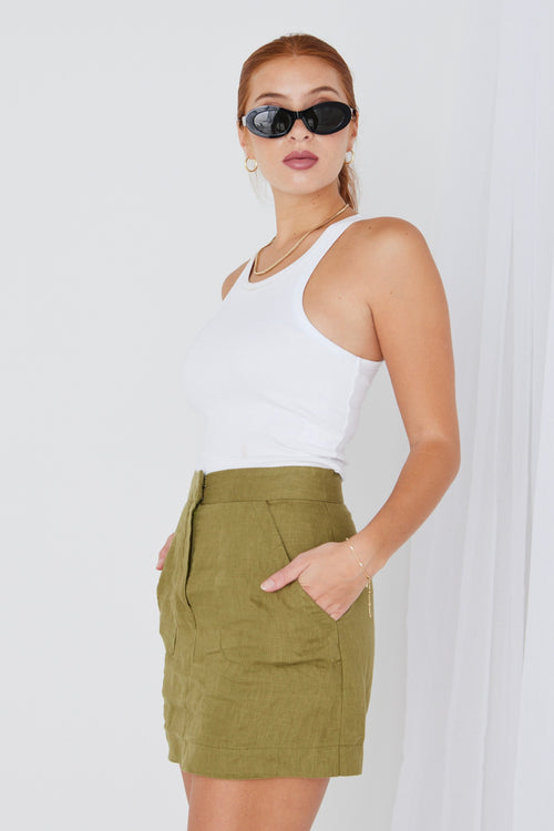 model wears white tank top and green linen mini skirt