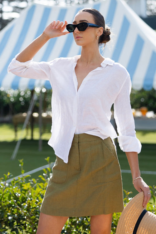 model wears a green linen mini skirt with a white shirt