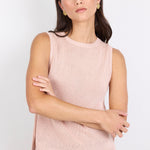 Woman wearing a light pink sleeveless top and blue jeans against a white background