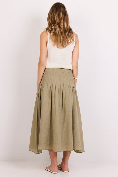 A woman shown from the back wearing a sleeveless white top and a pleated olive green midi skirt, standing against a plain white studio background.