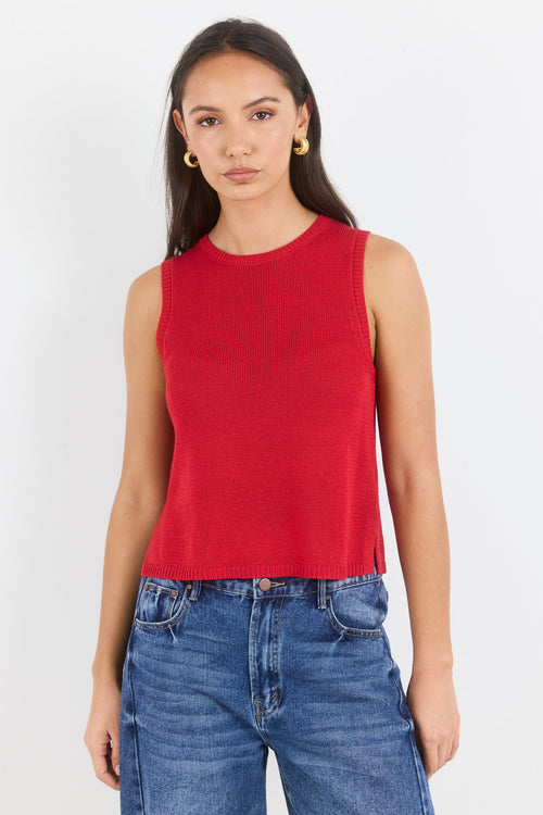 Woman wearing a red sleeveless top and blue jeans on a white background