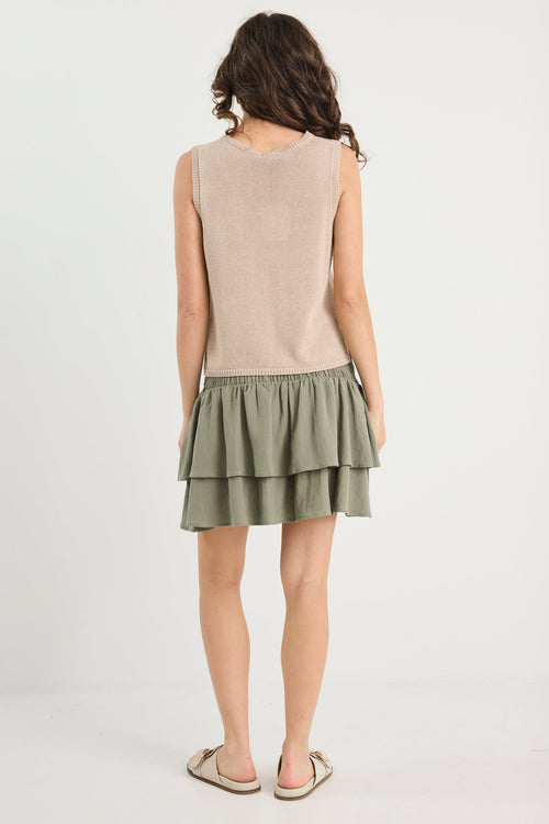 Woman wearing a beige sleeveless top and green tiered skirt on a white background