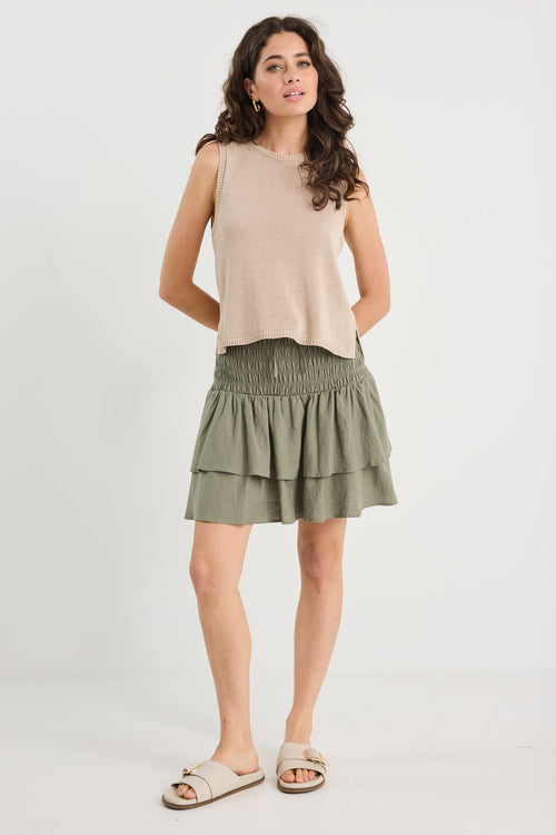 Woman wearing a beige sleeveless top and green skirt on a white background