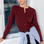Woman in a burgundy shirt leaning against a window with a white wall background