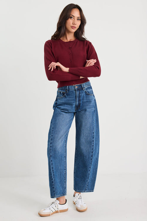 Woman wearing a burgundy sweater and blue jeans on a white background