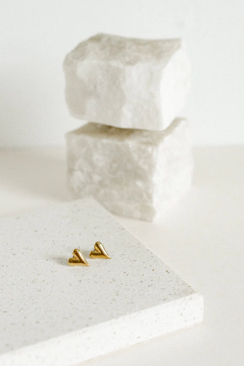 A pair of polished gold-toned heart-shaped stud earrings with a fluid, curved design and a slightly elongated point, giving a modern, sculptural look.