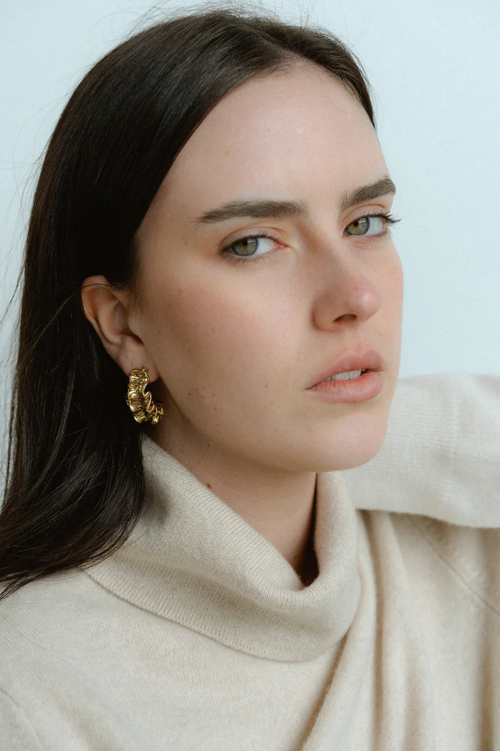 A pair of gold-toned hoop earrings with a unique ruffled design, featuring a textured, wavy surface that mimics soft fabric folds for a sculptural, organic look.