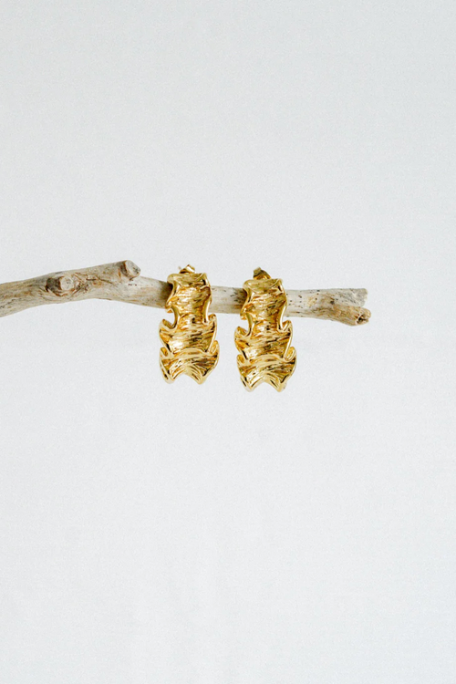 A pair of gold-toned hoop earrings with a unique ruffled design, featuring a textured, wavy surface that mimics soft fabric folds for a sculptural, organic look.
