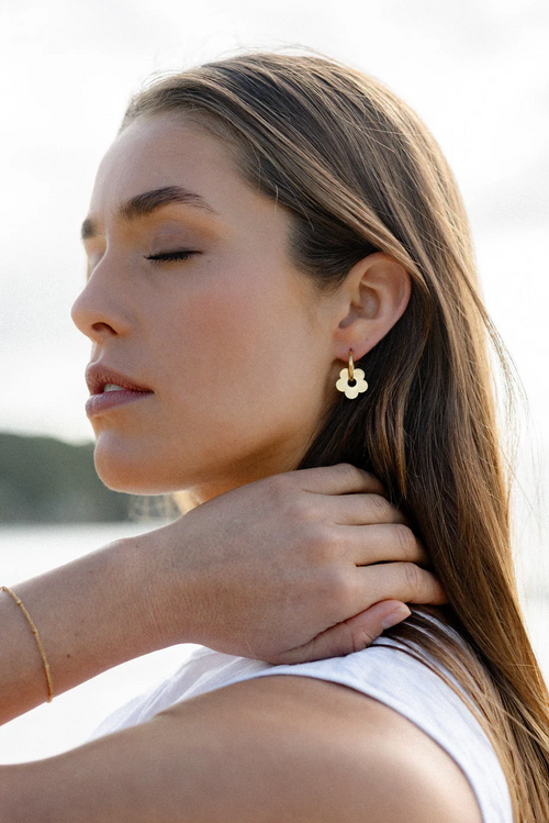 A pair of gold-toned hoop earrings featuring dangling flower-shaped charms with smooth, rounded petals and a high-shine finish