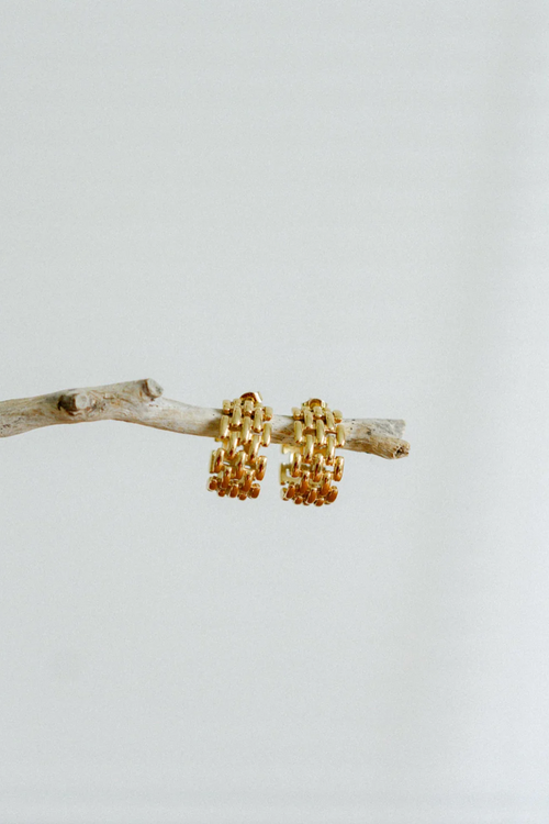 A pair of gold-toned hoop earrings featuring an intricate woven-link design, creating a bold, structured look with a glossy finish and open-back detail