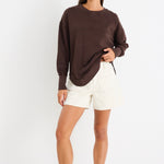 Relaxed-fit chocolate brown sweatshirt with tonal Re:Union embroidery, styled with cream shorts and gold hoop earrings.