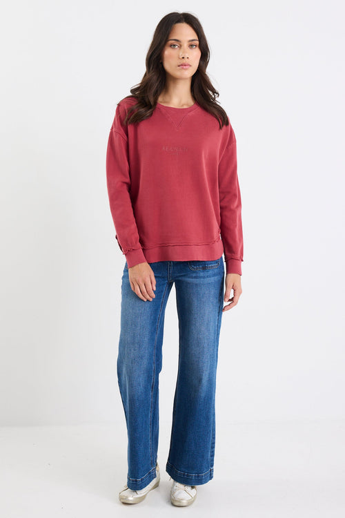 Woman wearing a red sweatshirt and blue jeans on a white background