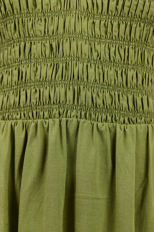 Close-up of an olive green smocked dress fabric, showing the detailed horizontal gathering and the gathered skirt section.