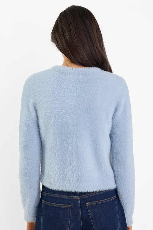 Person wearing a light blue sweater and dark jeans on a white background