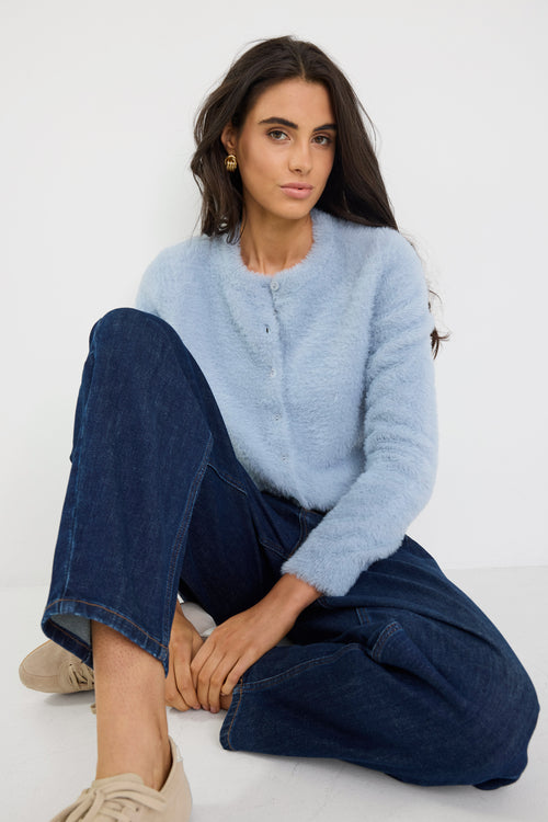 Woman wearing a light blue sweater and dark blue jeans sitting on a white background