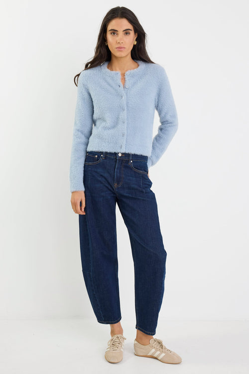 Woman wearing a light blue cardigan and dark blue jeans on a white background