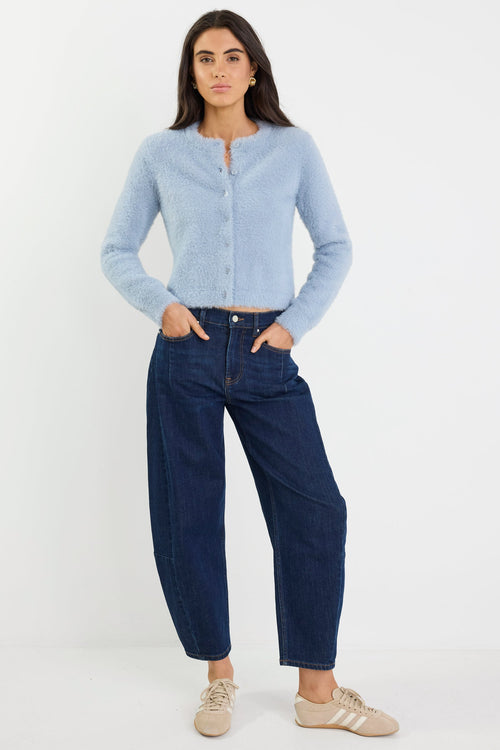 Woman wearing a light blue cardigan and dark blue jeans on a white background