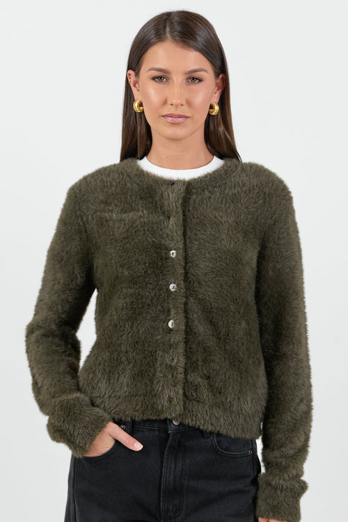 A woman wearing a soft, khaki fluffy cardigan with a round neckline and button-down front, paired with high-waisted black jeans.