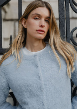 Woman wearing a light blue fuzzy sweater in front of an iron gate.