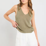 Woman wearing a green sleeveless top and white shorts on a light gray background