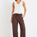 Woman wearing a white sleeveless top and brown wide-leg pants on a white background