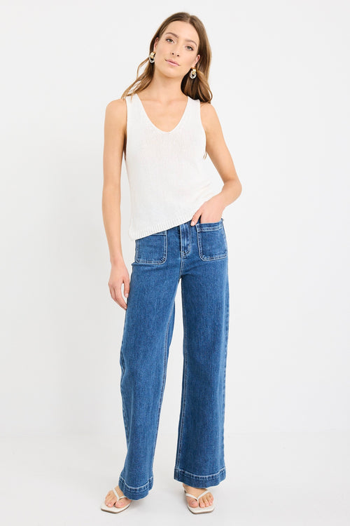 Woman wearing an ivory sleeveless knit vest top with a V-neckline, styled casually with blue jeans.