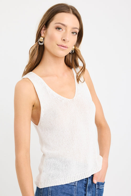 Woman wearing an ivory sleeveless knit vest top with a V-neckline, styled casually with blue jeans.