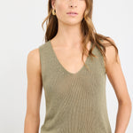 Woman wearing a sleeveless khaki knit top with a V neckline and relaxed fit, styled with light blue jeans.