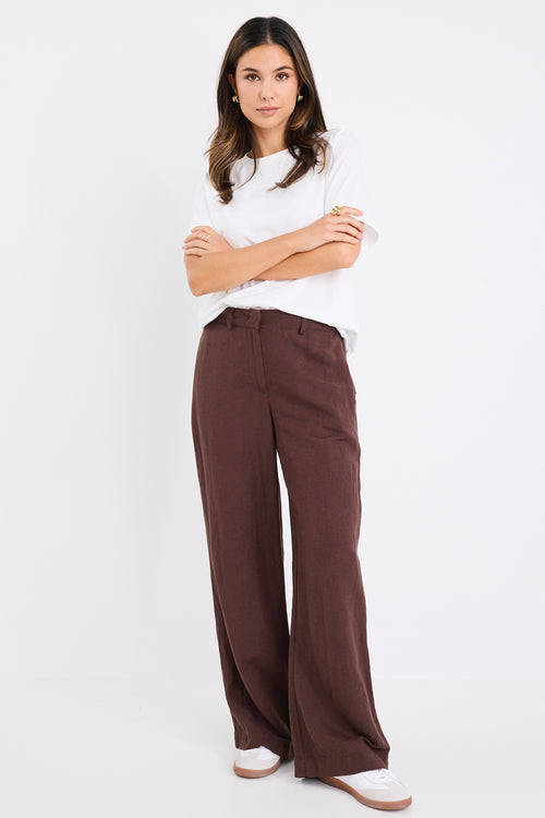 Woman wearing wide-leg chocolate brown trousers with a mid-rise waist.