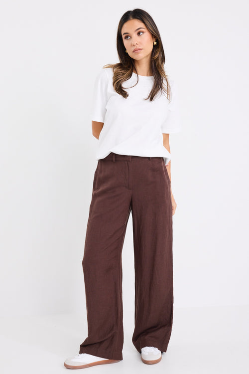 Woman wearing wide-leg chocolate brown trousers with a mid-rise waist.