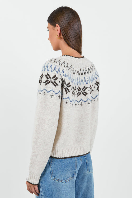 A woman wearing a cosy cream-colored cardigan with a Fair Isle pattern in shades of brown and blue, paired with high-waisted, relaxed-fit blue jeans.