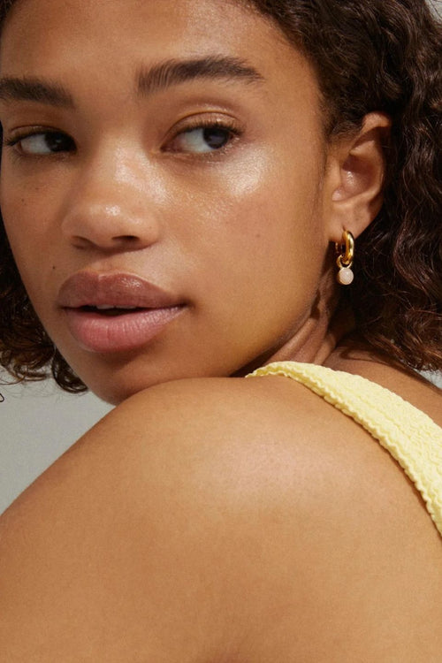 Close-up of a woman wearing a yellow top and gold earrings with a blurred background