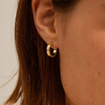 Close-up of a person wearing a gold hoop earring with a neutral background