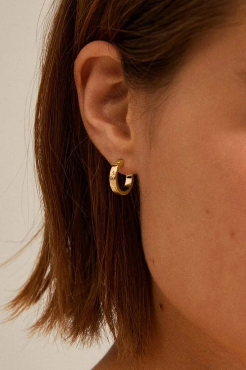 Close-up of a person wearing a gold hoop earring with a neutral background