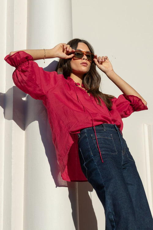 Woman wears a red top and blue jeans in the sun