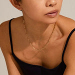Woman wearing a gold necklace against a neutral background