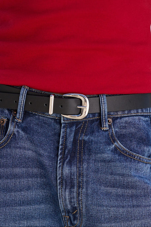 A close-up of a black leather belt with a silver-tone buckle worn over blue jeans and a red top.