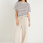 Woman in beige linen pants with side stripe detail and an elastic waistband, paired with a white stripe top. 